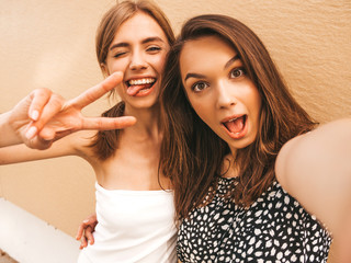 Two young smiling hipster women in summer clothes. Girls taking selfie self portrait photos on...