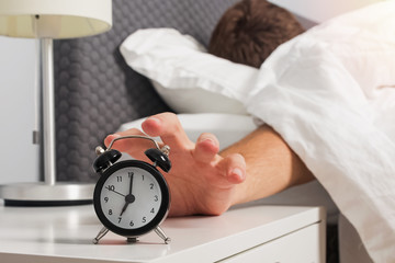 Man's hand reaching out alarm clock on the nightstand early in the morning.