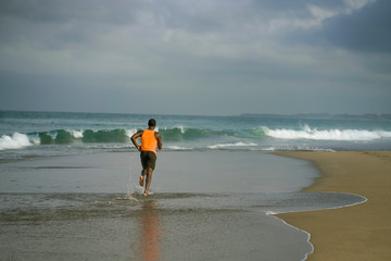 athletic full body portrait of young attractive and fit black afro American man running on the beach doing Summer fitness jogging workout at the sea in healthy lifestyle concept