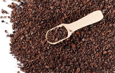 Chopped cocoa pile with wooden spoon isolated on white background, top view