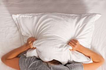 Woman lying in bed and covering her head with pillow.