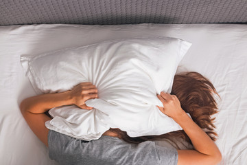 Woman lying in bed and covering her head with pillow.