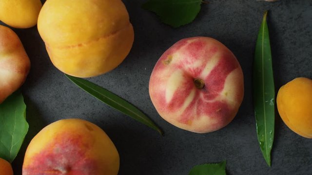 Nice yummy fresh apricots and peaches with green tree leaves on dark texture surface. Top view. Summer fruits. 4k.