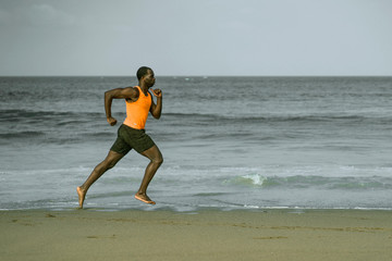 Fototapeta na wymiar athletic full body portrait of young attractive and fit black African American man running on the beach doing Summer fitness jogging workout at the sea in healthy lifestyle