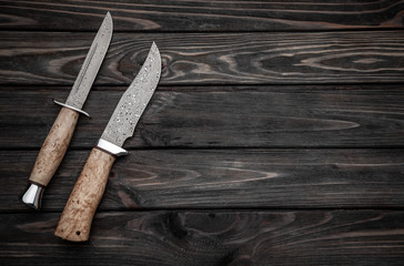 Hunting bowie knife with a wooden handle on dark wooden background. Steel arms weapon. top view