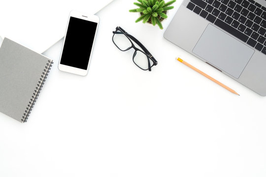 Creative flat lay photo of workspace desk. Top view office desk with laptop, glasses, phone, pencil, notebook and plant on white color background. Top view with copy space, flat lay photography.