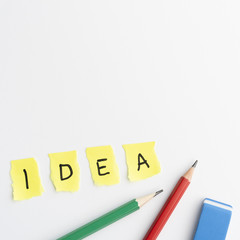 Idea text on torn yellow pieces paper with pencils and eraser over white background