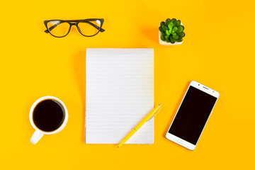 Notebook, phone, mobile, coffee, pen, glasses on a yellow background. Copy space. Top view. Mockup