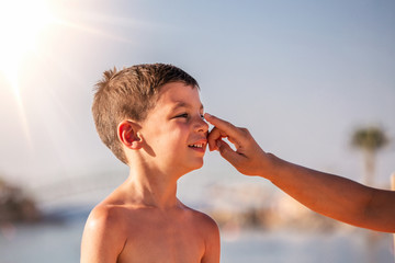 Mother applying sunblock cream on son face. Mother put sunblock cream on little boy face at beach