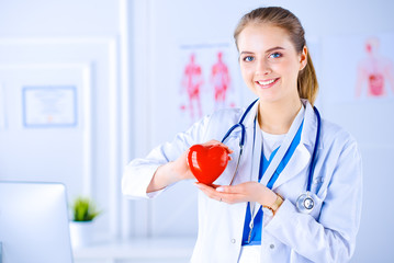 Female doctor with stethoscope holding heart, on light background. Health, medicine, people and cardiology concept