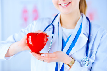 Female doctor with stethoscope holding heart, on light background. Health, medicine, people and...