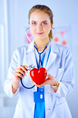 Female doctor with stethoscope examining red heart. Health, medicine, people and cardiology concept