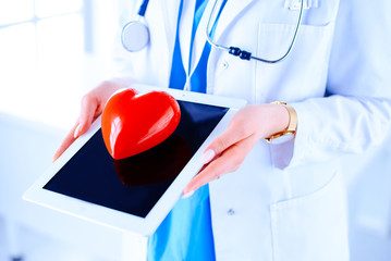 Doctor cardiologist with stethoscope using digital tablet and holding red heart. Health, medicine,...