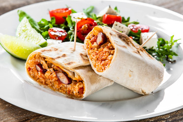 Burrito with vegetable salad on white plate