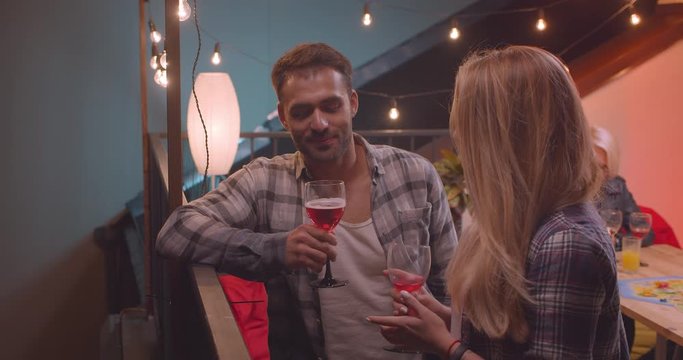Closeup portrait of attractive amn and woman standing talking happily with diverse group of friends on background at party with fairy lights