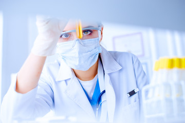 Female scientist explore a test tube with liquid in a laboratory. Researcher is surrounded by medical vials and flasks