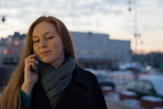 Young woman in polto calls on the phone on the street