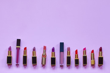 Many colorful opened lipsticks, setting in a raw on bright lilac background.. Chic design, red, lilac and nude tones. Copy space for any text, close up.