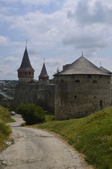 Fototapeta na wymiar Castle on the hill. The wall and towers of the magic fortress in Kamyanets-Podilsky in Ukraine against the background of a blue-haired sky and green grass