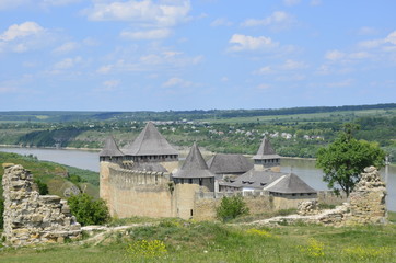Fototapeta na wymiar Magic Khotun fortress in Ukraine against the background of a blue-haired sky and white clouds, and green grass, trees and Dniester river