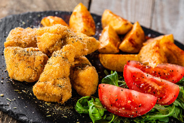 Fried chicken nuggets, baked potatoes and vegetable salad