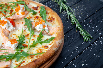 Top view pizza with salmon, arugula, red caviar, cheese on dark wooden background with copy sapce. Italian pizza with seafood. Food background. Tasty homemade italian cuisine pizza