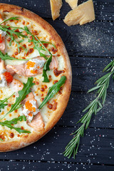 Top view pizza with salmon, arugula, red caviar, cheese on dark wooden background with copy sapce. Italian pizza with seafood. Food background. Tasty homemade italian cuisine pizza