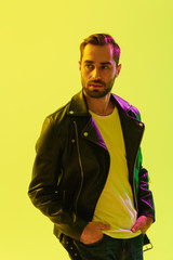 Handsome young stylish man posing isolated over light green background wall with led neon lights dressed in leather jacket.