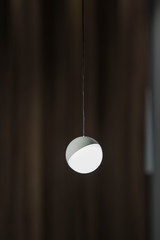 A small chandelier in the shape of a ball, with a warm light, minimalistic lamp. On dark background