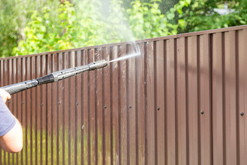 Cleaning fence with high pressure power washer, cleaning dirty wall.