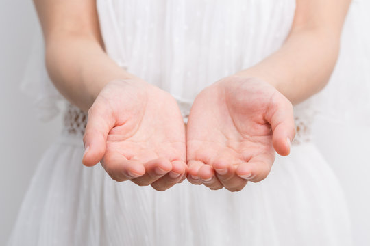 Woman hands cupped together against white dress.
