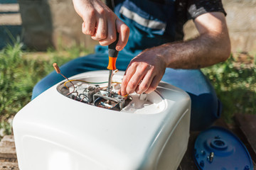 Repair and maintenance of the water heater. A man twists a screwdriver element of the water heater. Outdoor