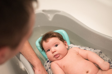 father bathes daughter. portrait of a baby is being bathed by his father using tub at home