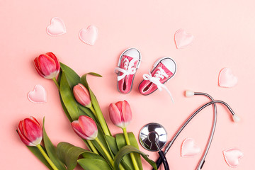 Bunch of tulips with stethoscope and baby girl shoes on pink background.