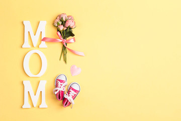 Word mom with pink baby girl sneakers and small bouquet of roses on a yellow background.