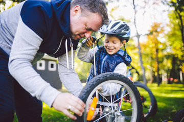 Father's day Caucasian dad and 5 year old son in the backyard near the house on the green grass on the lawn repairing a bicycle, pumping a bicycle wheel. Dad teaches how to repair a child's bike