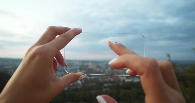 Girl in both hands holding horizontal mobile mockup gadget against modern cityscape. Close-up female tourist using futuristic smartphone observing urban horizon view in highland.