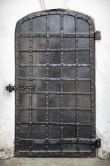 Ancient church door on a white wall. Old black metal door of the church with rivets.