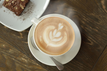 Hot coffee, milk foam, smoke in a white cup and snacks on a wooden table in a popular cafe