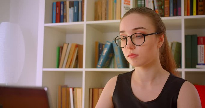 Closeup portrait of young successful redhead businesswoman in glasses using laptop in office indoors