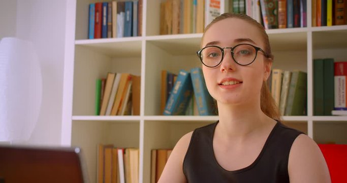 Closeup portrait of young successful redhead businesswoman in glasses using laptop looking at camera smiling happily in office indoors