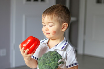 Little boy with atopic dermatitis on his cheek holding sweet red pepper and fresh broccoli in his...