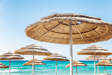 Thatched sun umbrellas on the beach against the background of the turquoise sea and clear blue sky.
