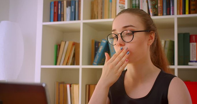 Closeup portrait of young redhead businesswoman in glasses using laptop yawning being sleepy in office indoors