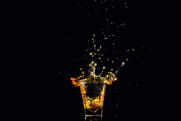 Isolated shot of whiskey with splash on black background, brandy in a glass