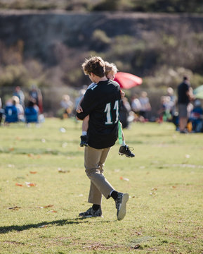 Boy carrying his little brother off a football field after an injury, California, United States