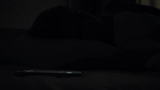 Sleepy woman turns alarm off while awakening in the morning.