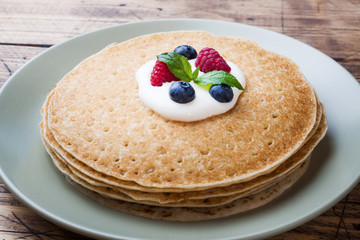 Plate of delicious thin pancakes with berries on wooden table Copy space