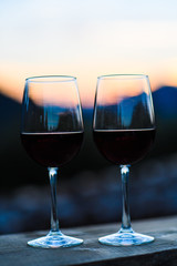 Two glasses of wine at sunset dramatic sky on mountain landscape background