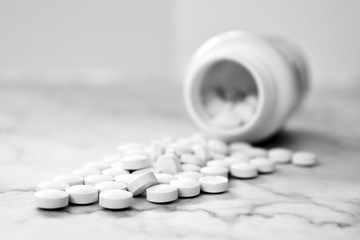 Many white medical pills spilling from a plastic medicine bottle container on light background